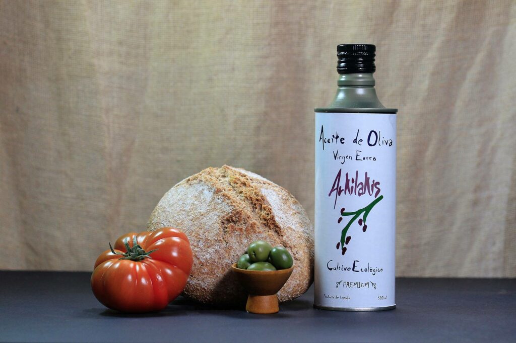 Botella AOVE Premium 500 ml Arkilakis junto a aceitunas, hogaza de pan y tomate