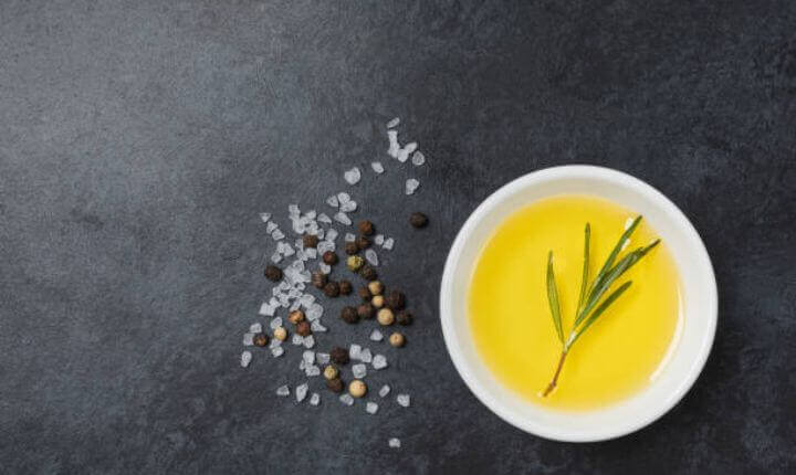 Un tipo de aceite de oliva virgen extra en un plato con una hoja del olivo dentro del plato y con sal y pimienta esparcidos al lado del plato